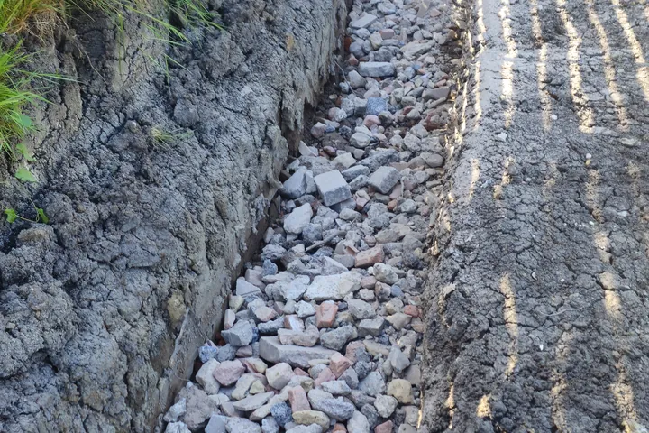 Stone-filled drainage trench beside a boundary fence